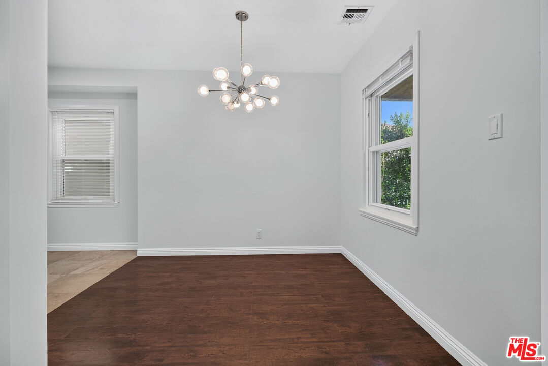 Empty dining room with dark wood floors, two windows, and a modern branching chandelier.
