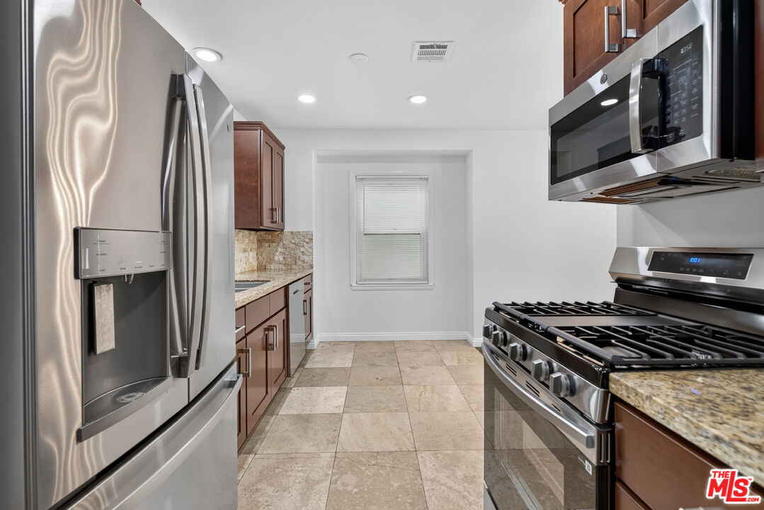 Kitchen with stainless steel appliances, dark wood cabinets, stone counters, and tiled floor.
