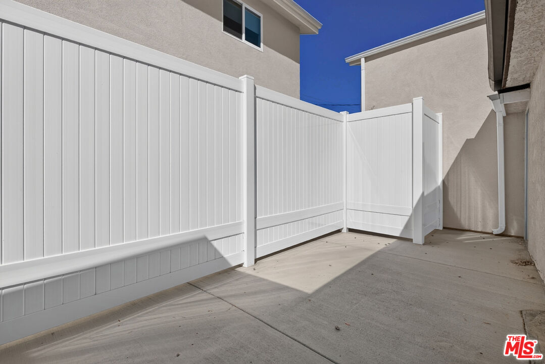 Concrete side patio enclosed by a tall white vinyl privacy fence beside a stucco home.