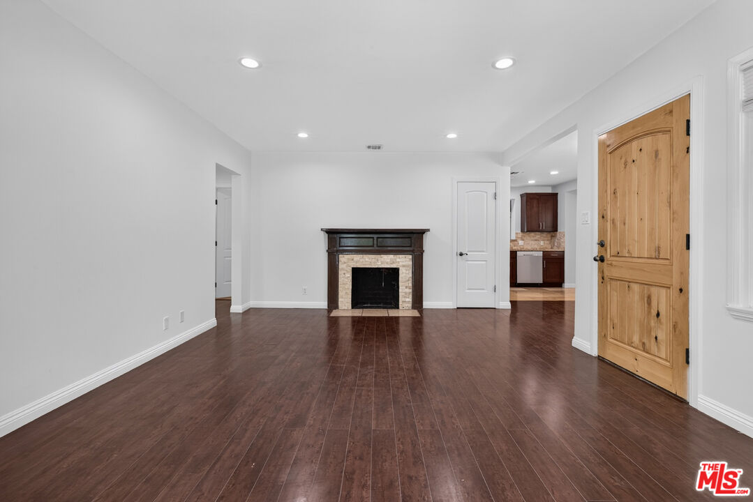 Vacant living room with dark hardwood floors, a stone-surround fireplace, and a prominent wood front door.