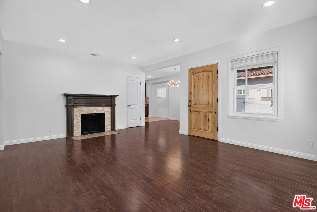 Empty living room with dark wood floors, stone fireplace, and a wooden entry door.