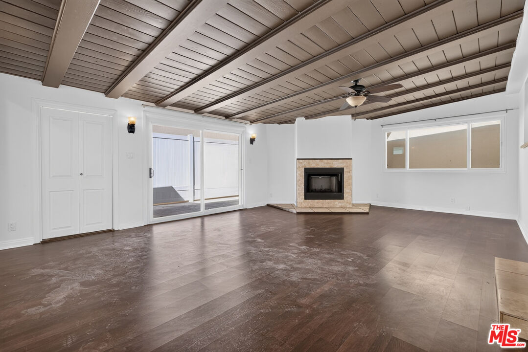 Empty living room with exposed-beam ceiling, stone-trimmed fireplace, and sliding glass doors.