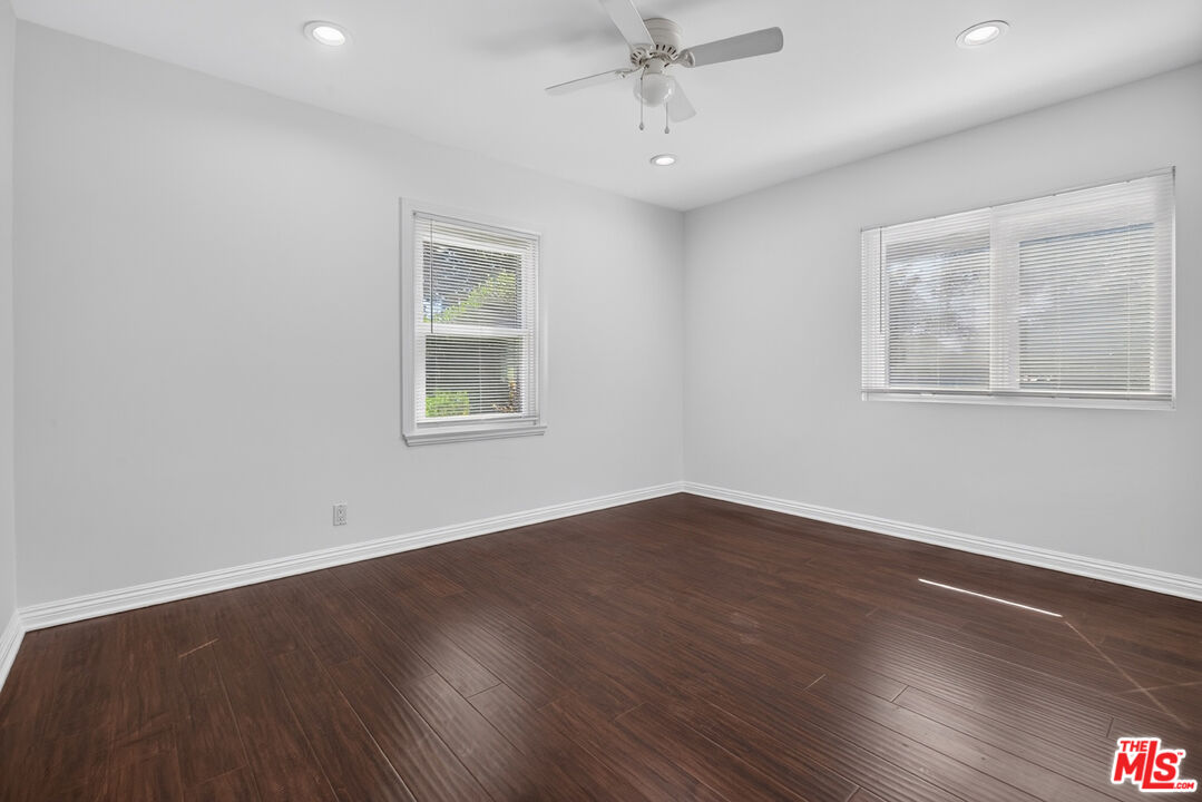Empty room with dark wood flooring, two windows with blinds, and a ceiling fan.