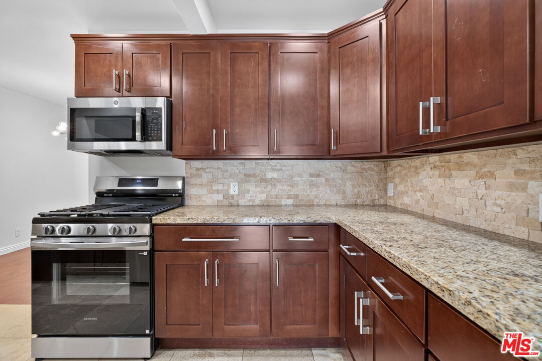 Kitchen with dark wood cabinets, granite counters, stone backsplash, and stainless steel appliances.