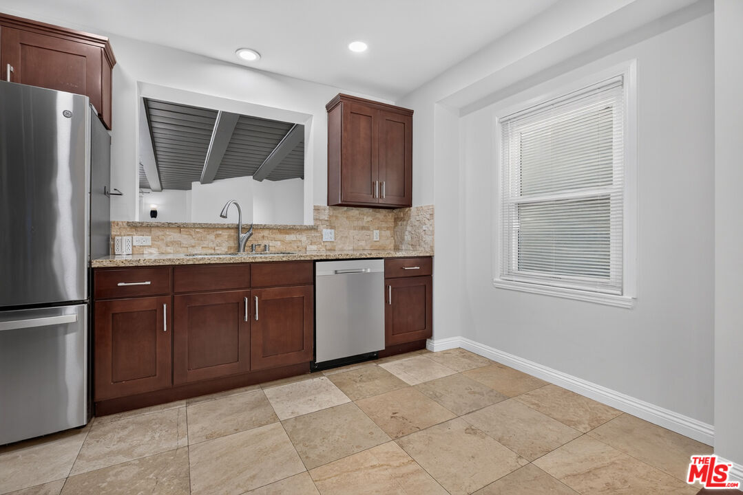 Kitchen with dark wood cabinets, stainless steel appliances, stone backsplash, and beige tile flooring.