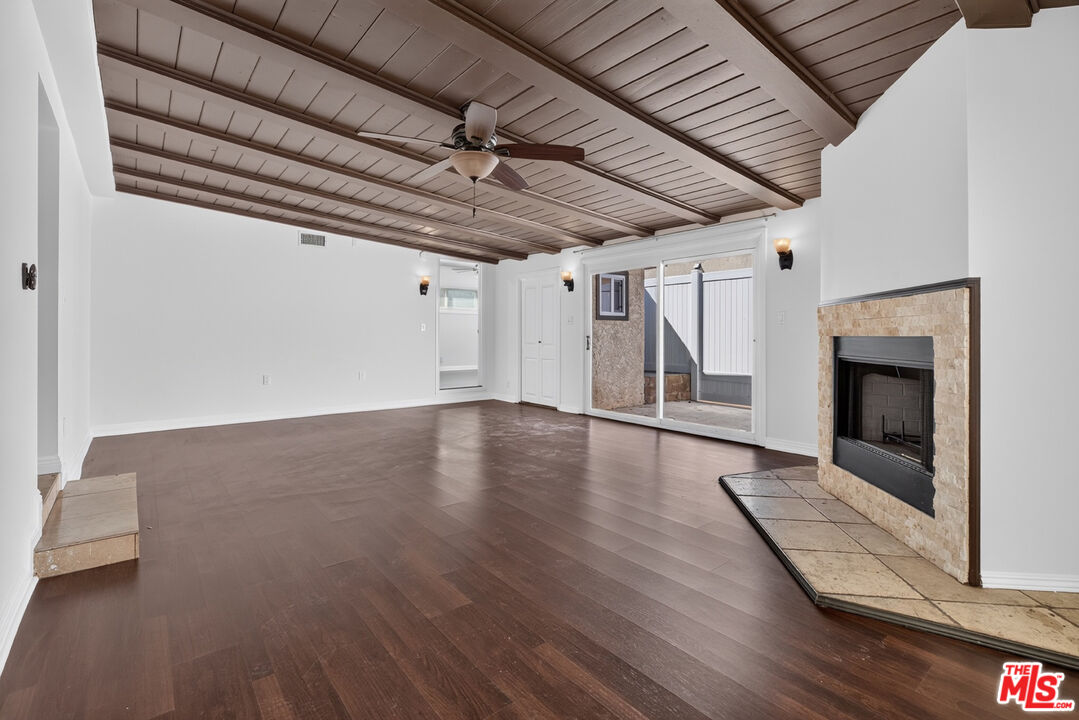 Living room with a vaulted wood ceiling, dark floors, and a stone fireplace beside sliding patio doors.