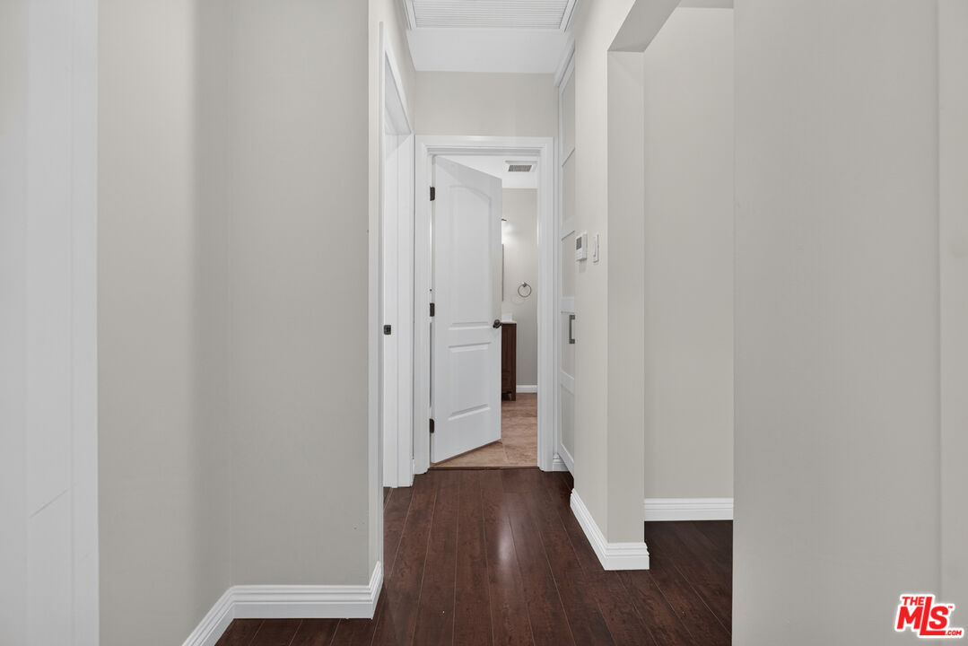 Hallway with dark hardwood floors and an open doorway to a tiled room.