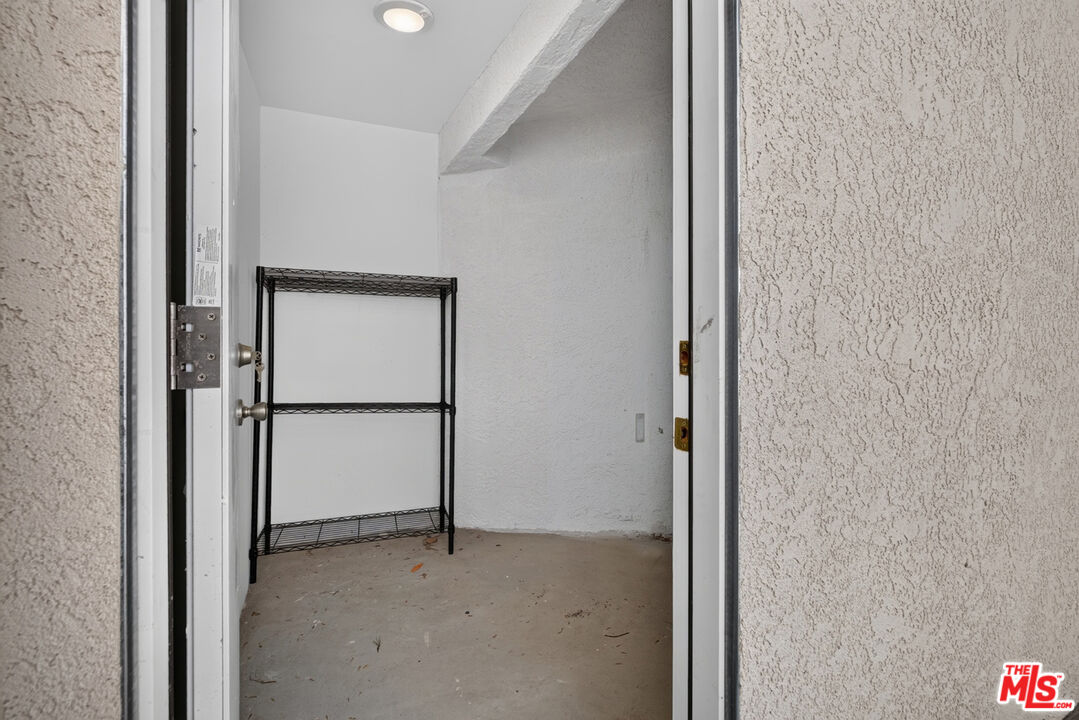 Small vacant storage room with white textured walls and a black wire shelving unit.