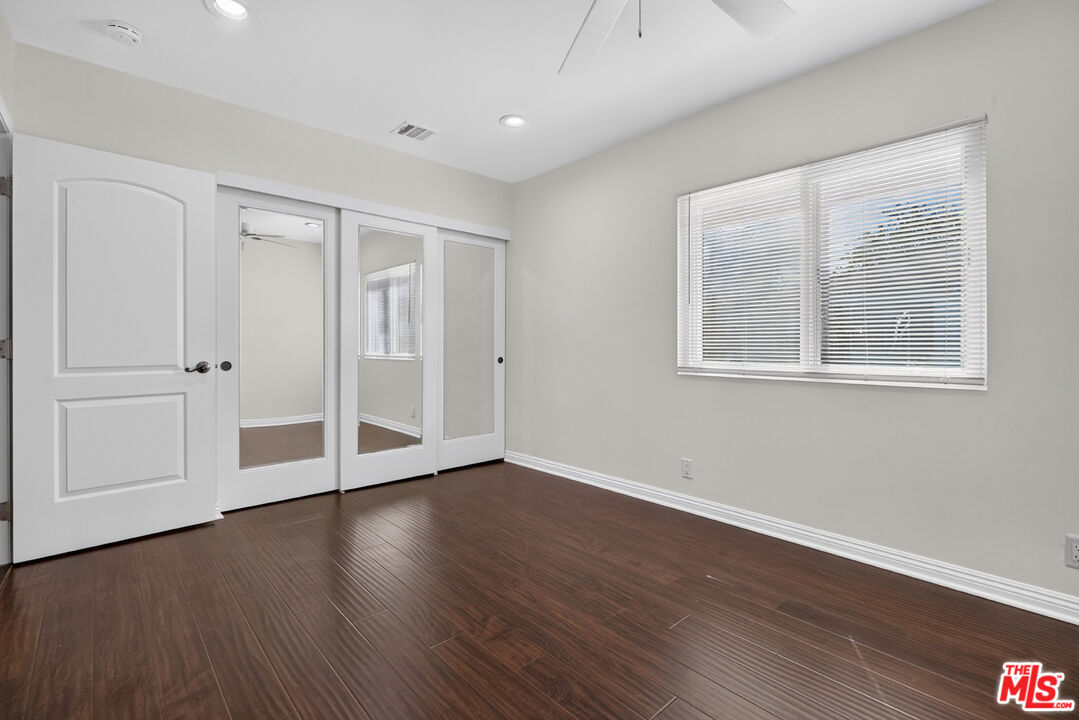 Empty room with mirrored closet doors, a wide window with blinds, and dark wood-look flooring.