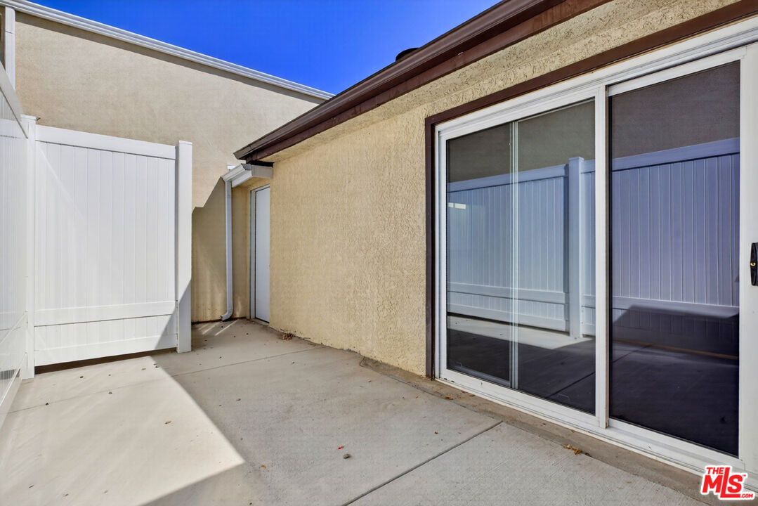 Concrete patio beside beige stucco walls, with white privacy fencing and sliding glass doors.