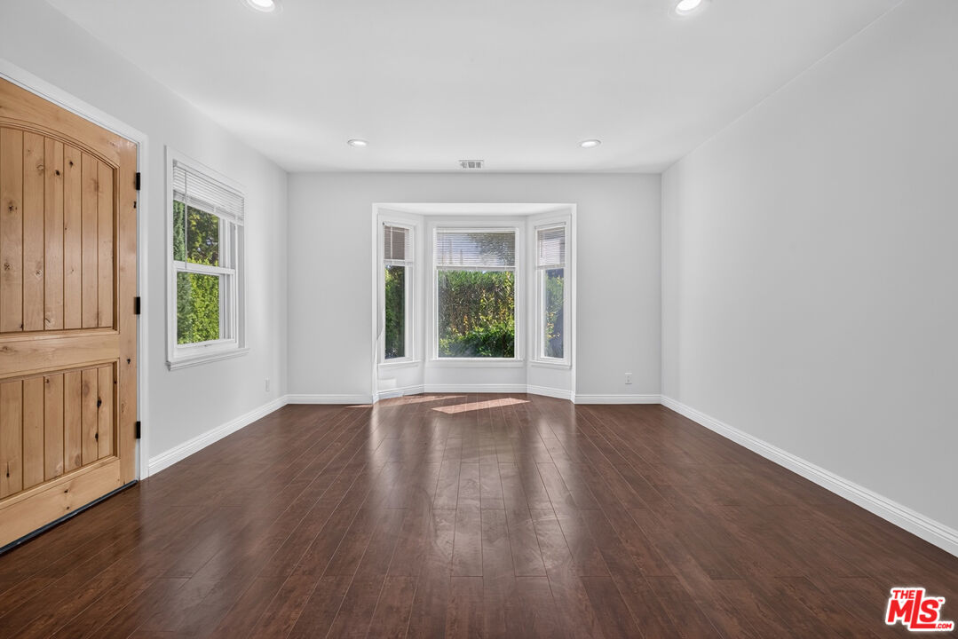 Empty room with dark wood floors, a rustic wooden door, and a bay window.