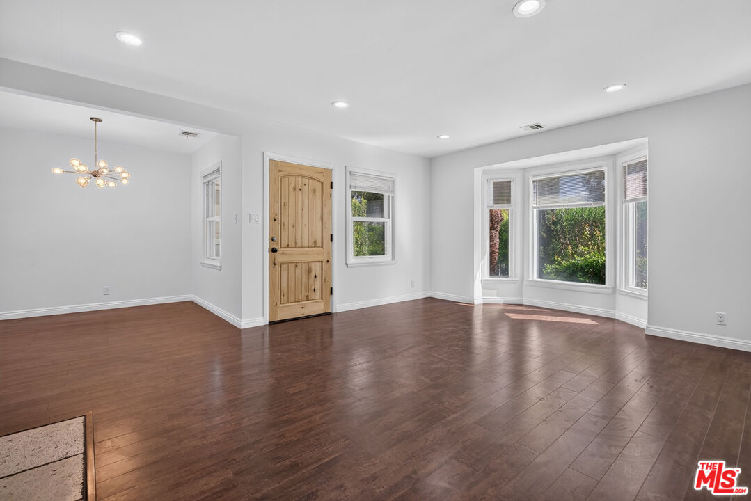 Vacant living and dining area with dark hardwood floors, a wooden front door, and a bay window.