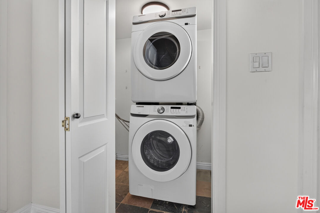 Stacked front-loading washer and dryer in a laundry closet with dark tile flooring.