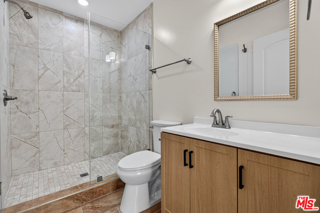Bathroom with a marble-look tiled shower, glass enclosure, and wood-front vanity.