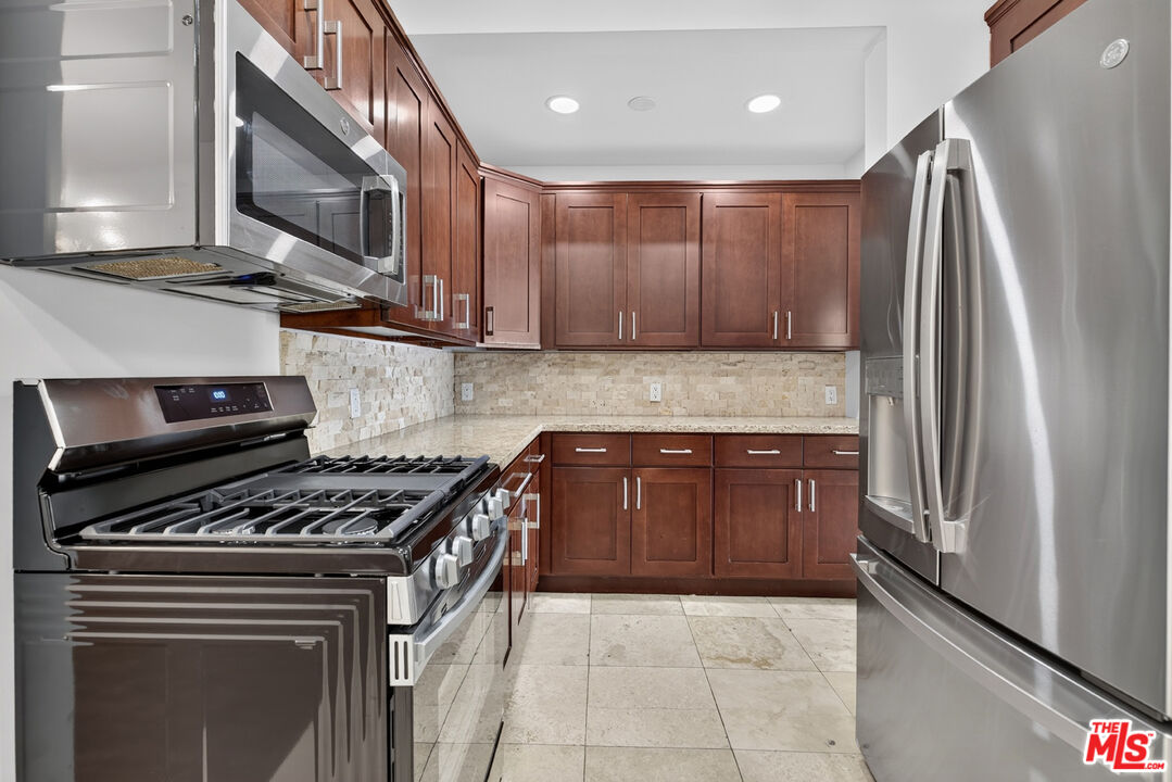 Kitchen with reddish-brown cabinets, stone backsplash, and stainless steel appliances.