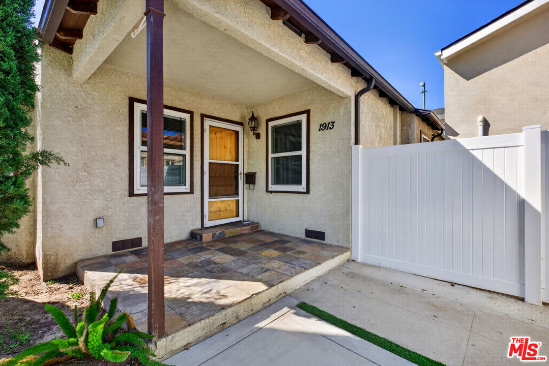 Stucco home with a covered tiled porch, wooden front door, and white privacy fence.