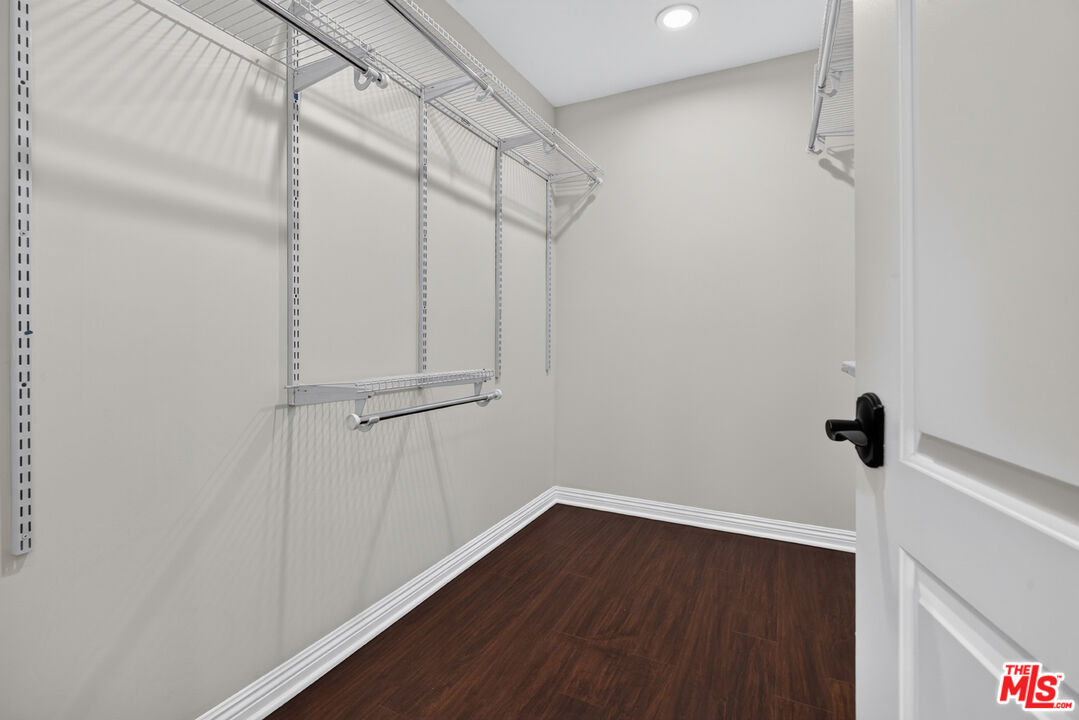 Walk-in closet with white wire shelving, hanging rods, and a dark wood floor.