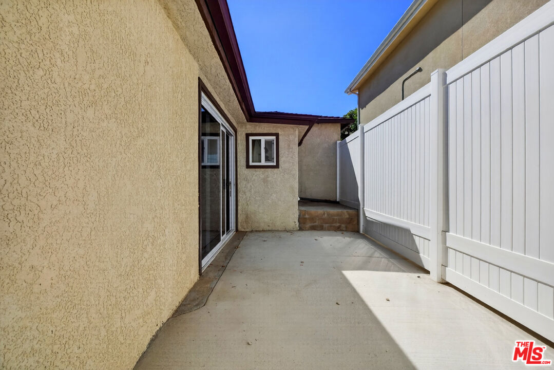 Concrete side patio beside a stucco house, enclosed by a tall white privacy fence.