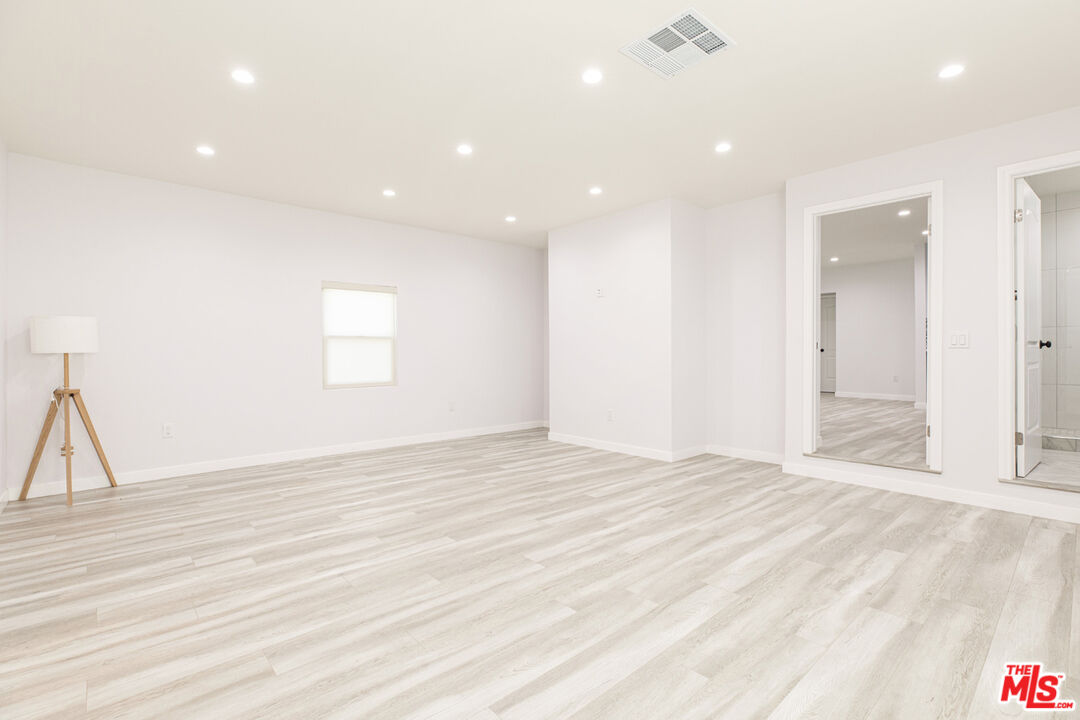 Bright empty room with pale plank flooring, recessed lights, and a doorway to an adjoining bathroom.