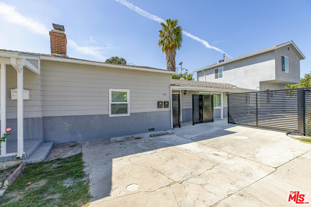 Gray-sided property with a gated entrance and concrete driveway beneath a tall palm tree.