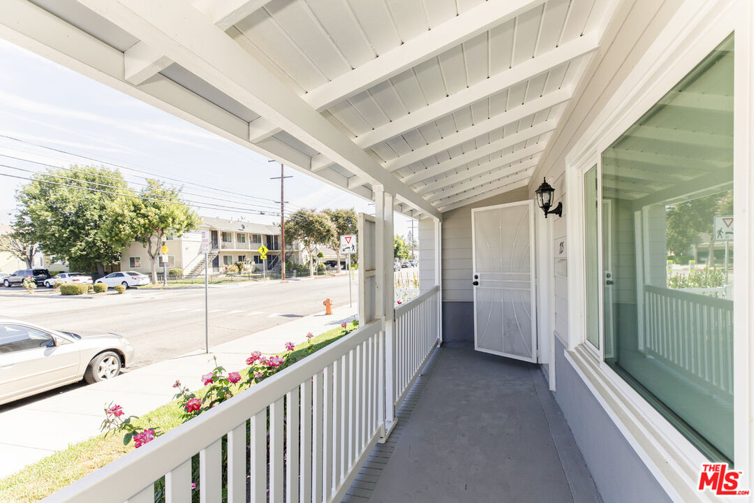 Covered front porch with white railings, an open screen door, and pink flowers beside the sidewalk.