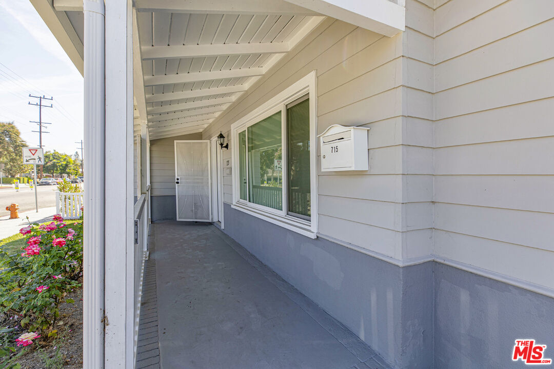 Covered front porch with a screen door, large windows, and pink flowers beside the walkway.