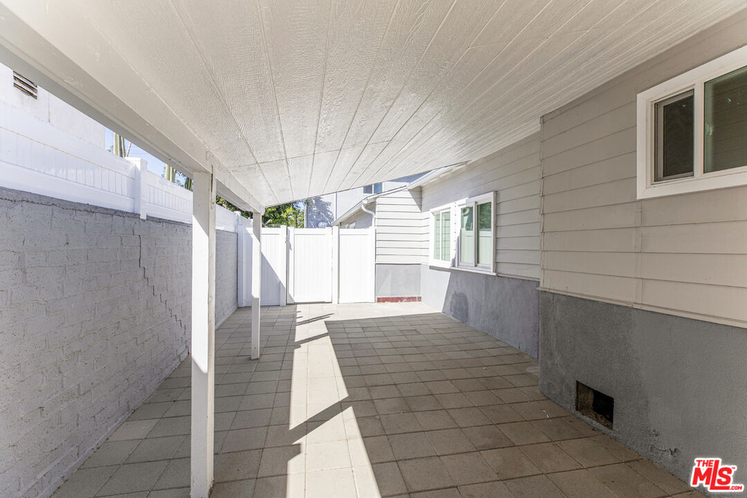Covered tiled patio with white posts, a privacy fence, and house windows.