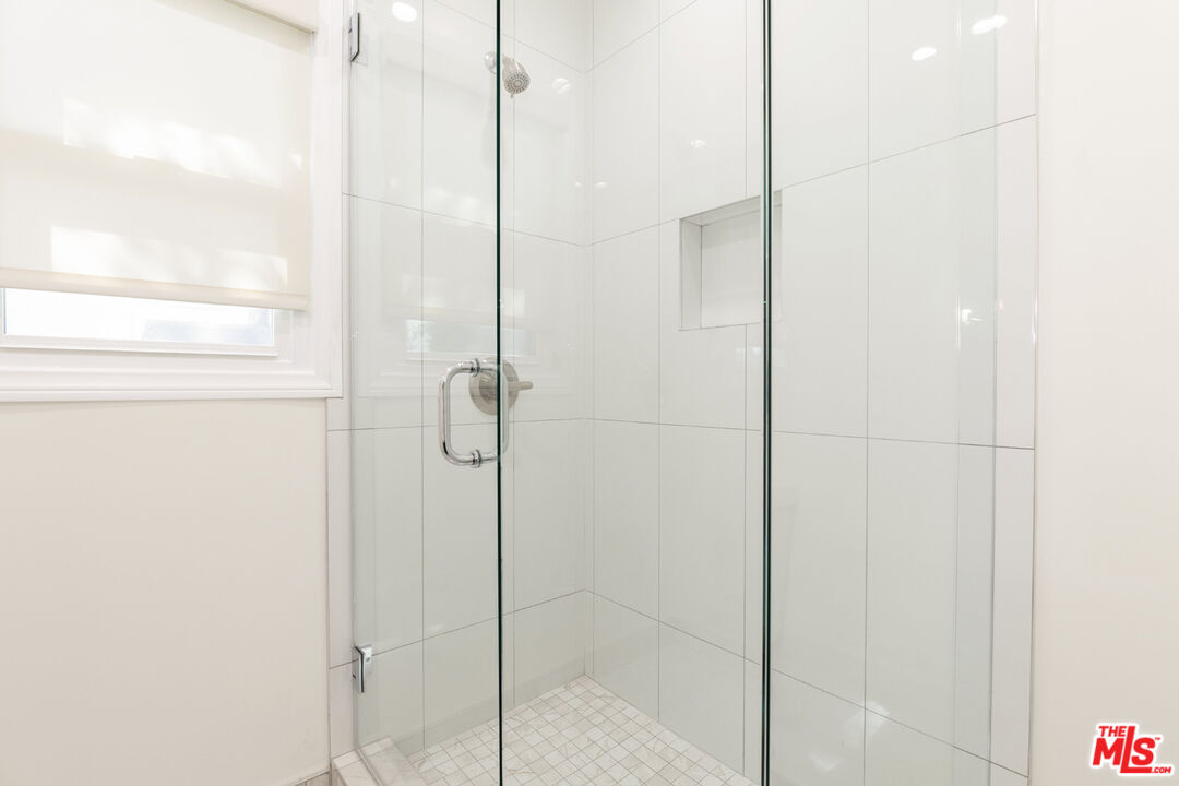 Walk-in shower with a glass enclosure, white tile, recessed niche, and window.