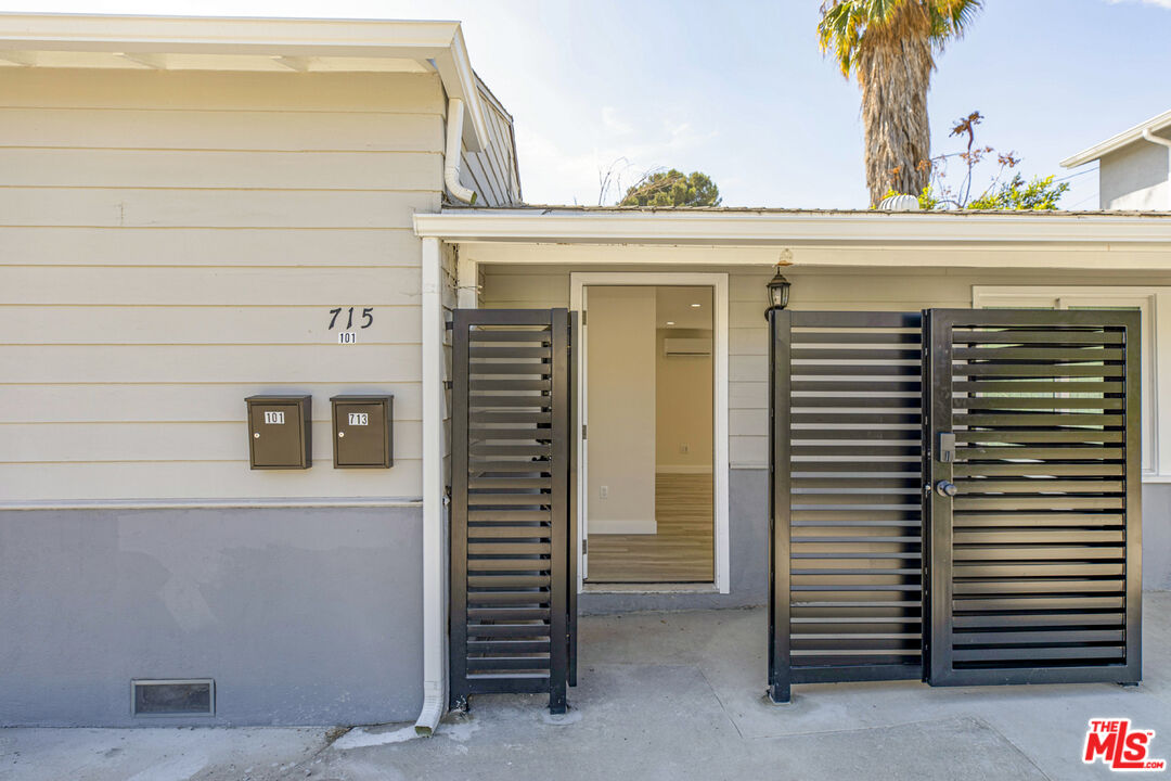 Property entrance with an open black slat gate, two mailboxes, and an empty interior visible through the doorway.