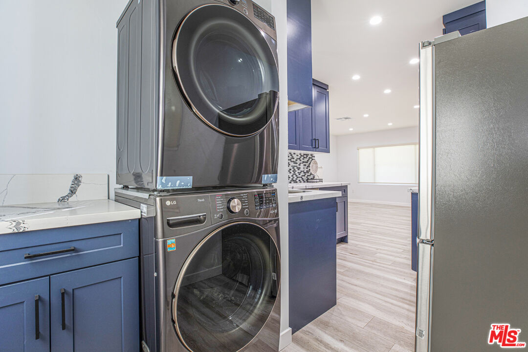 Laundry area with stacked stainless-steel washer and dryer beside blue cabinetry, opening onto the kitchen.