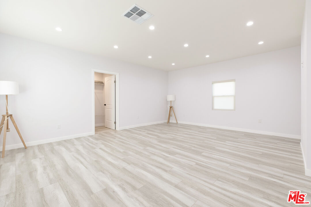 Empty bedroom with pale plank flooring, recessed lights, and an open closet.