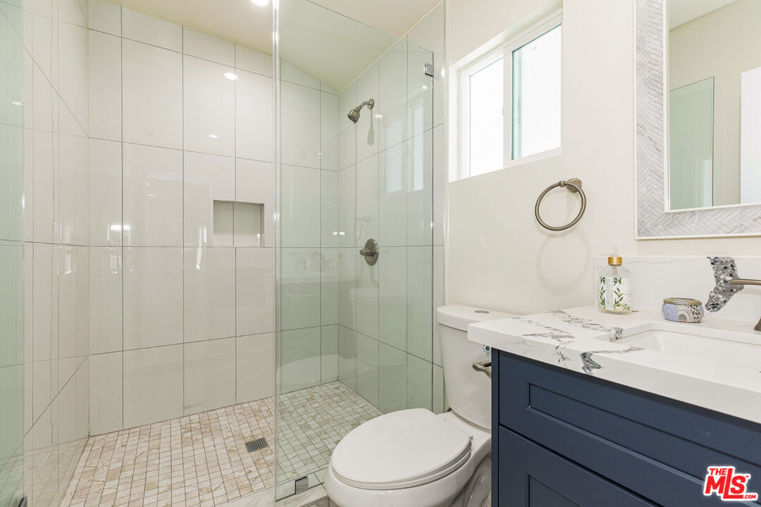 Bathroom with a glass-enclosed tiled shower and navy vanity with marble-look countertop.