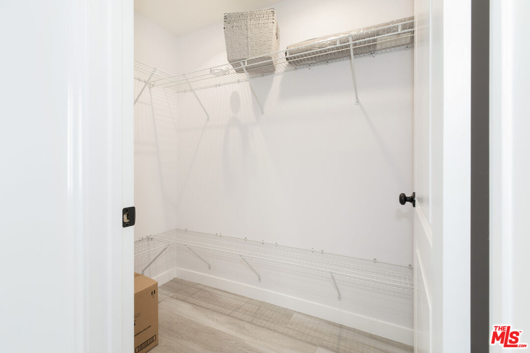 Walk-in closet with white wire shelves, light wood flooring, and a woven basket.