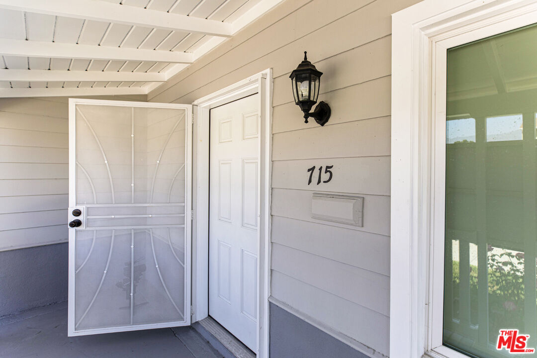 Covered home entry with an open white security screen door and the number 715 on gray siding.