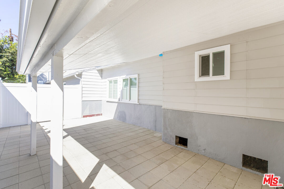 Covered tiled patio beside a white-sided house, with support posts and a privacy fence.