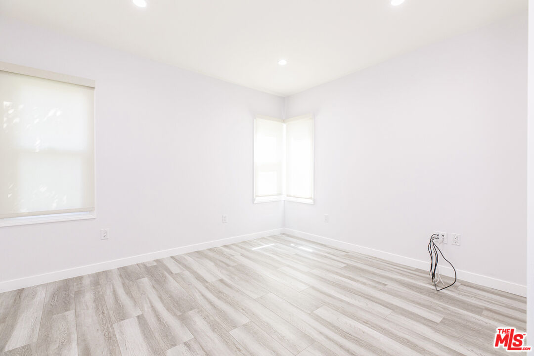 Empty bright room with corner windows, recessed lights, and light wood-look flooring.