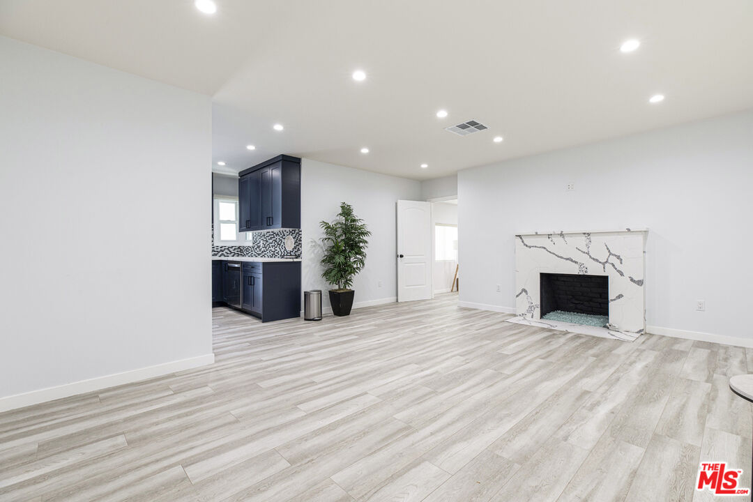 Empty living room with light wood-look floors, a marble-look fireplace, and navy kitchen cabinets.