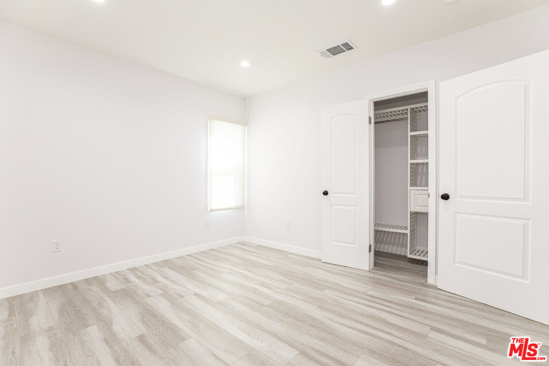 Empty bedroom with pale wood-look flooring and an open closet with built-in shelving.