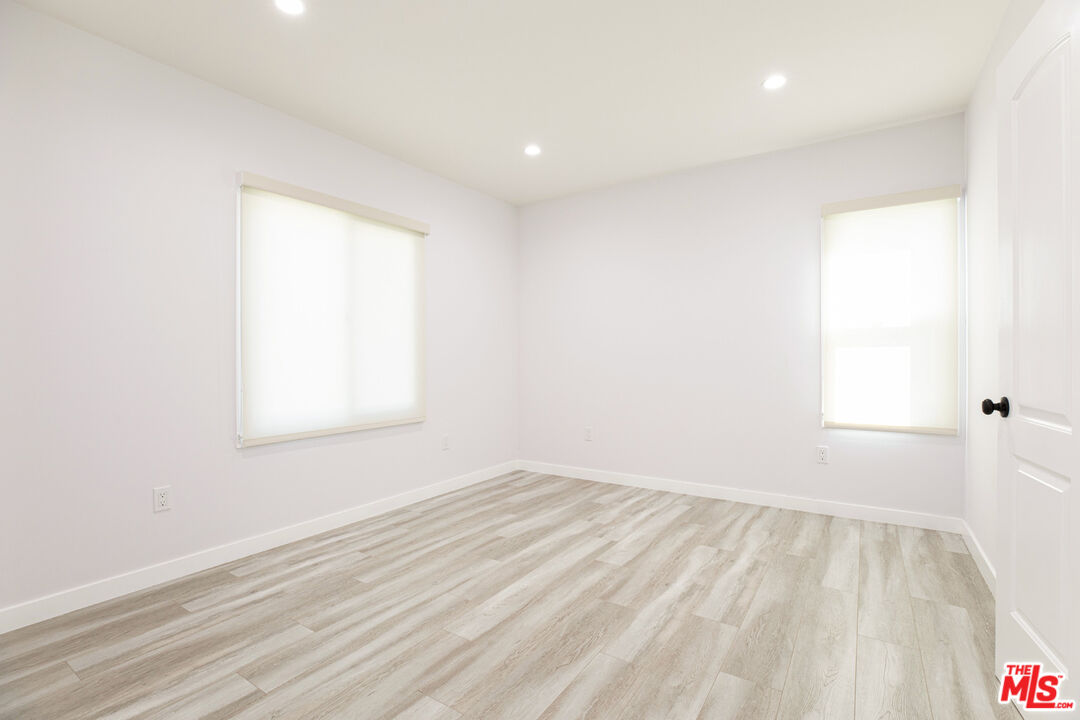Empty room with light wood-look flooring, two shaded windows, and recessed ceiling lights.