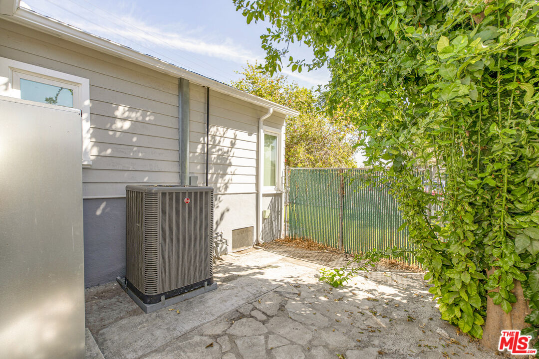 Side of a gray-sided house with an outdoor air-conditioning unit beside a green fence.