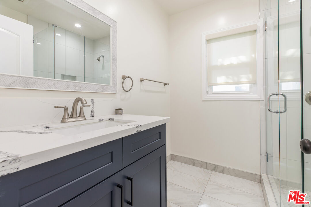 Bathroom with dark vanity, marble-pattern countertop and floor, and a glass-enclosed shower.