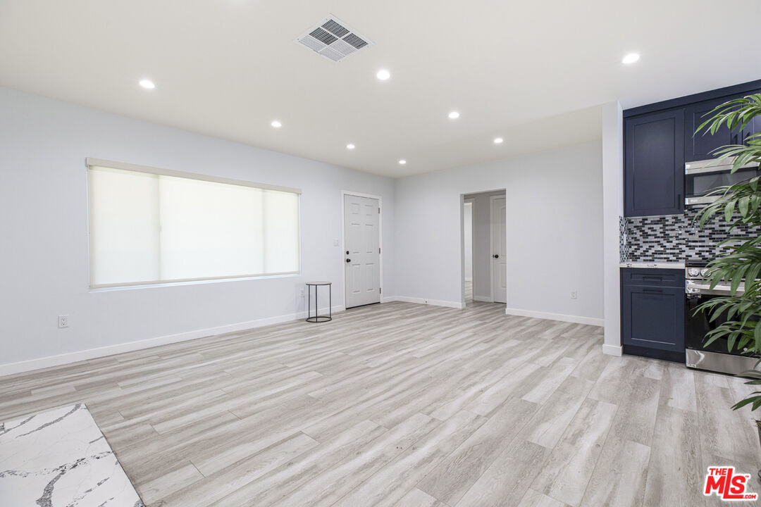 Empty living area with light wood-look floors beside a navy-blue kitchen.