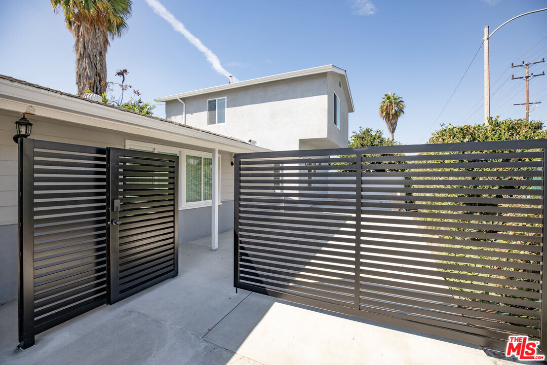 Home entry courtyard with black horizontal-slat gates and a white modern house beyond.