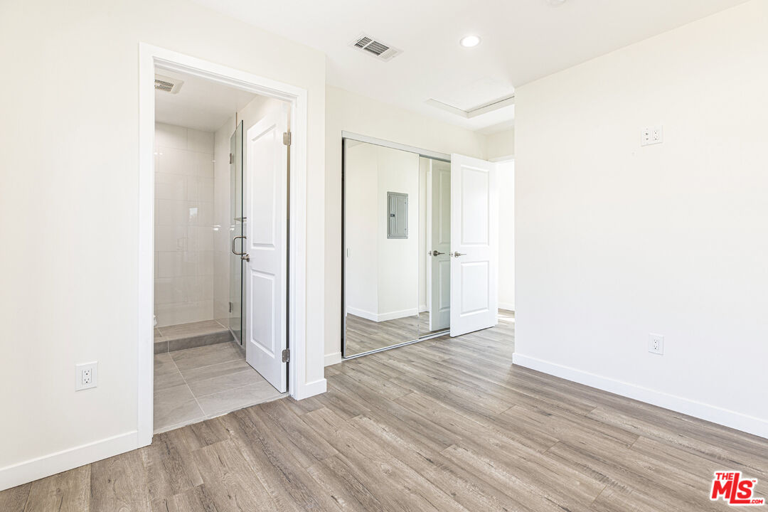 Vacant room with gray wood-look floors, mirrored closet doors, and an adjoining tiled shower.