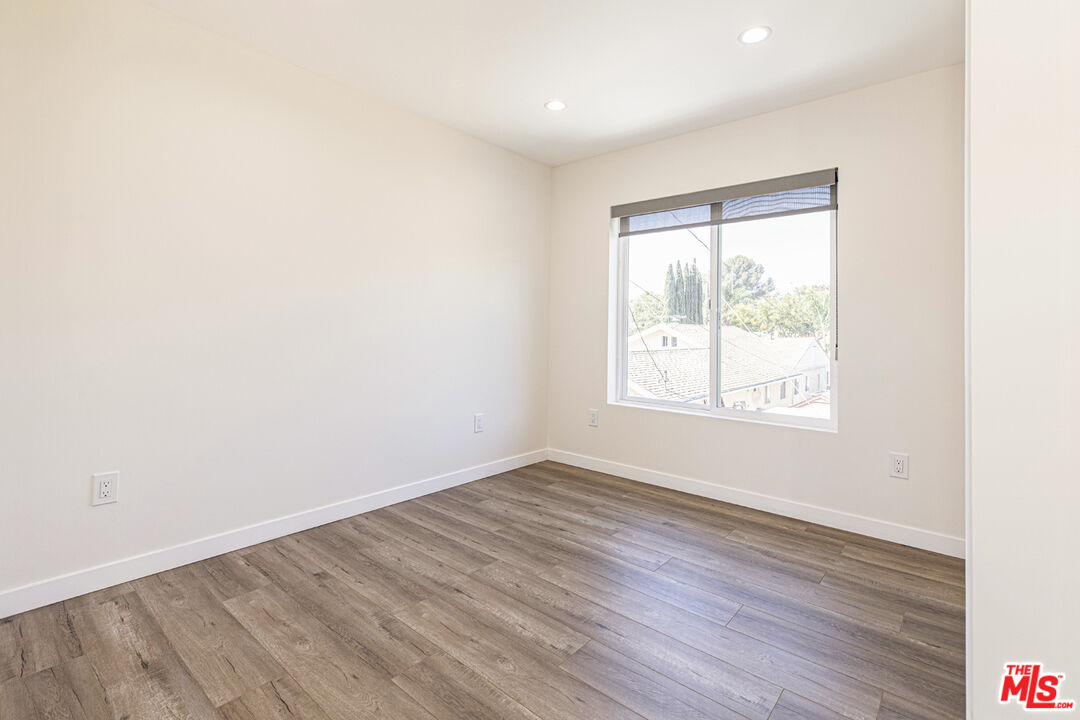Empty room with gray-brown plank flooring and a large window overlooking rooftops and trees.