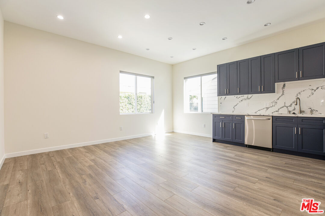 Vacant kitchen with dark blue cabinets, marble backsplash, and wood-look flooring.