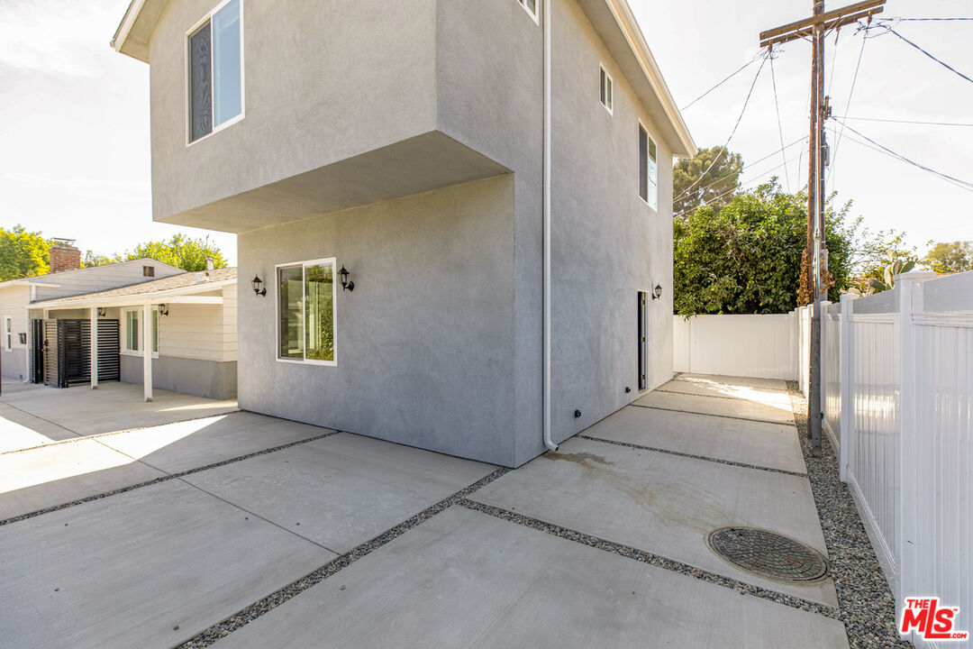 Modern two-story gray stucco home beside a broad concrete driveway and white privacy fence.
