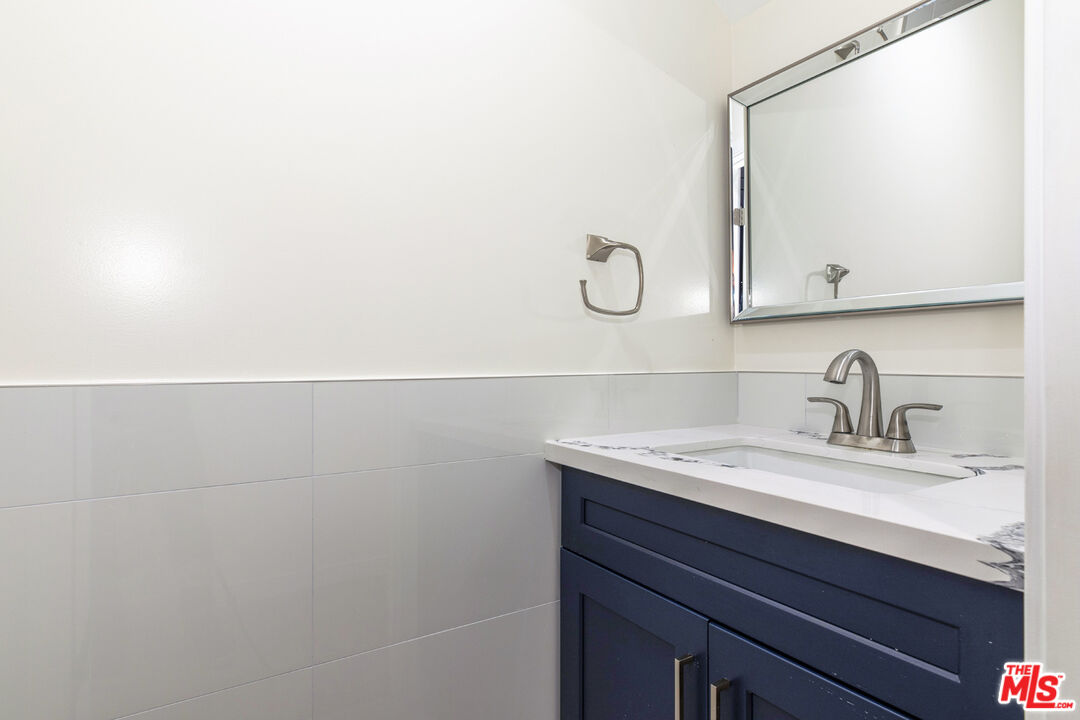 Bathroom vanity with navy cabinetry, a white marble-look counter, and a large mirror.