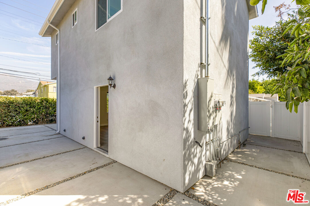 Two-story stucco house with a side entrance, exterior utility equipment, and a gated concrete side yard.