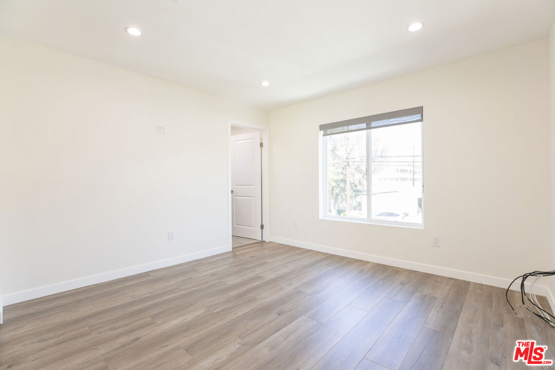 Empty renovated room with light plank flooring, recessed lights, and a large window with a gray shade.